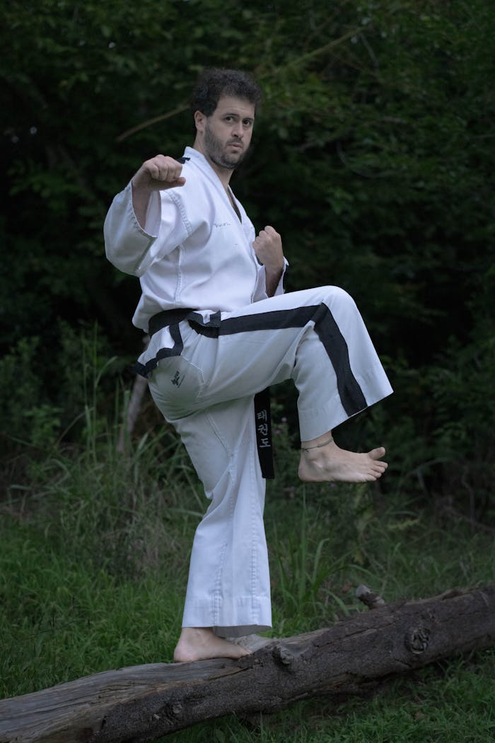 who-we-are Martial artist striking a pose in a traditional gi, set against a lush outdoor backdrop.