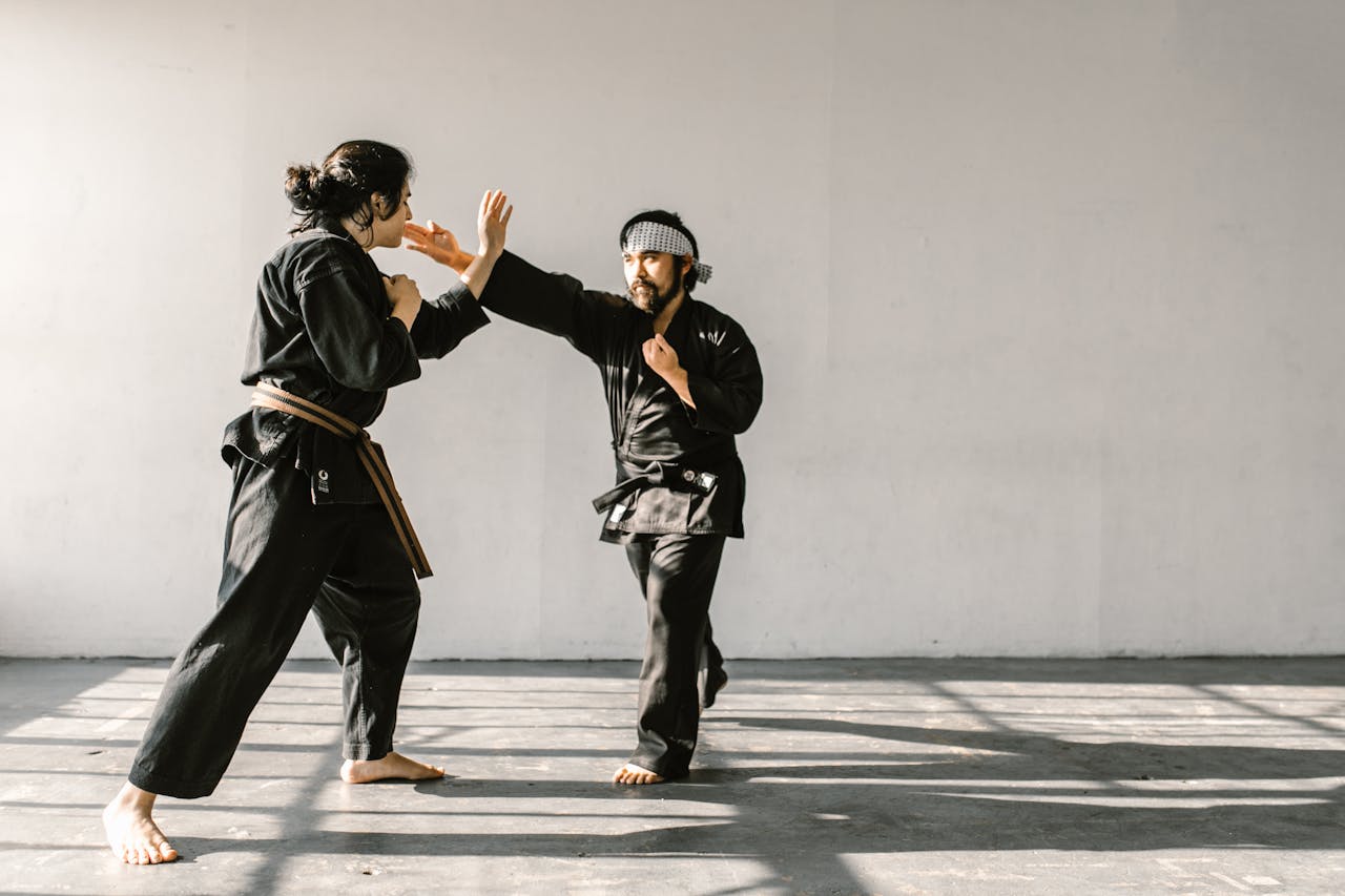 our-story Two martial artists sparring in an indoor dojo wearing traditional black attire.