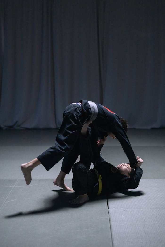 Two men engaged in intense Brazilian Jiu Jitsu sparring match indoors.